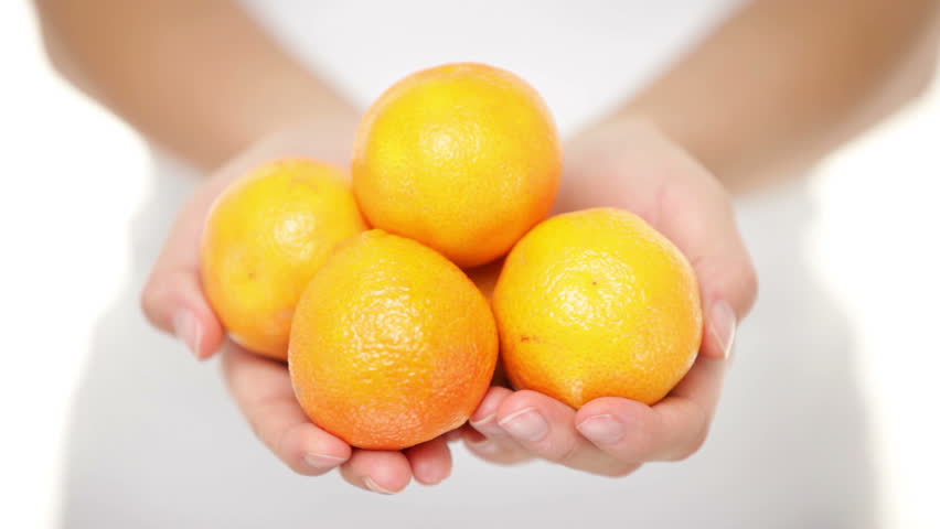 Clementine. Clementines that are a variety of mandarin oranges citrus fruits. Woman showing handful moving them into focus. Shot in studio with shallow depth of field.