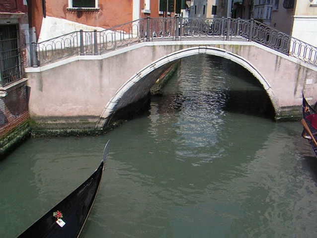 Venice: Typical Gondola boat along a canal, moving under a bridge
