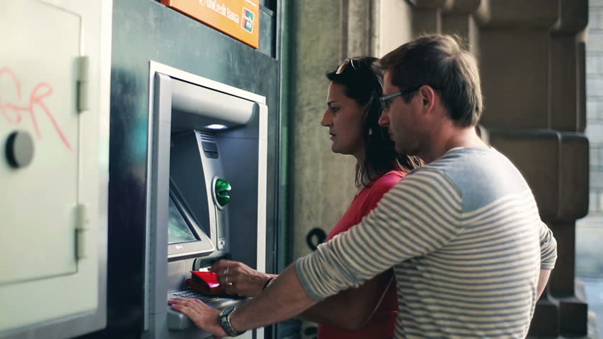 Young couple withdrawing money from an ATM, steadycam shot
