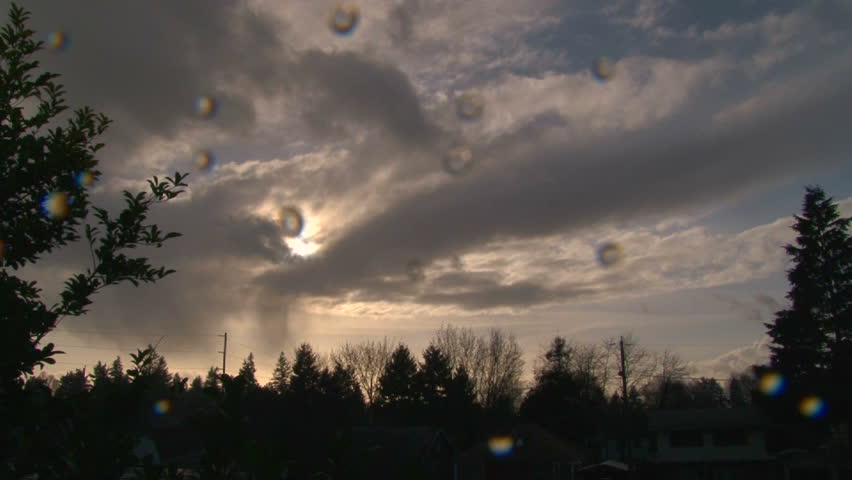 Time lapse during sunset with rain clouds building around sun and rain falling on camera lens.
