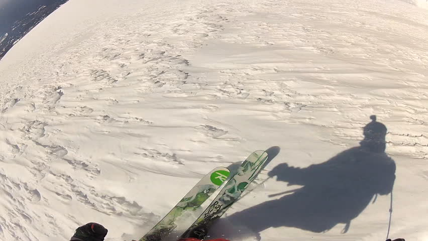 A skier carves back and forth as he rides down a mountain covered in fresh powder during the day. It is shot with a camera mounted to the athletes head and provides a POV, point of view, perspective.