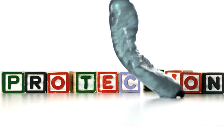 Condom filled with water falling and bouncing in front of blocks spelling protection in slow motion