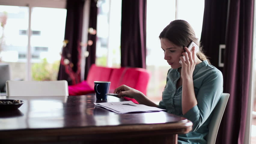 Young businesswoman with cellphone and documents working in home
