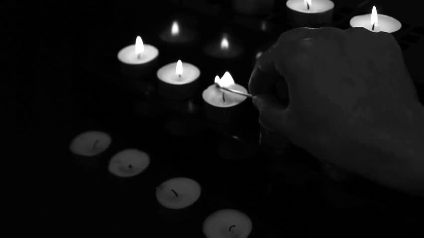 Hand using match to light candles for worship in black and white