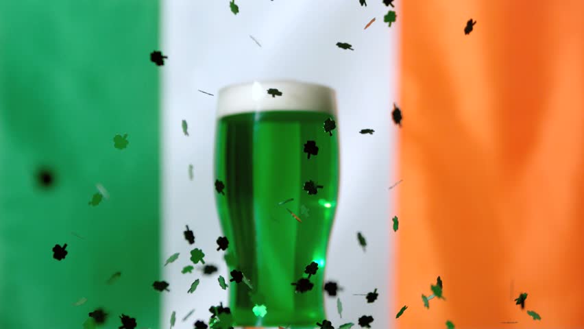 Shamrock confetti falling in front of green pint on irish flag background in slow motion