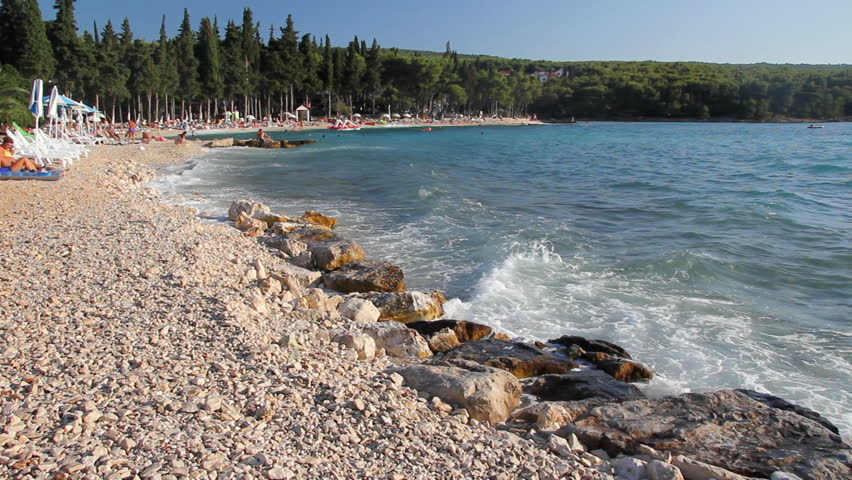 Waves splashing the beach, people sunbathe and enjoy on vacation, island Brac in Croatia