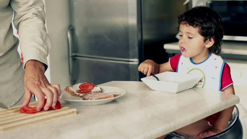 Little boy eating cornflakes with milk, father preparing sandwich, slow motion shot at 240fps
