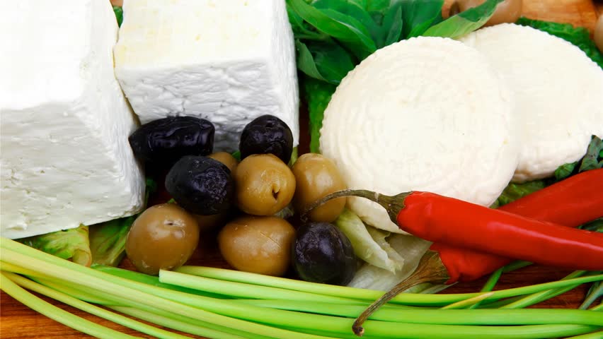 dairy food : feta white cheese cubes and round served on wooden cut plate with green leaves and olive oil isolated over white background