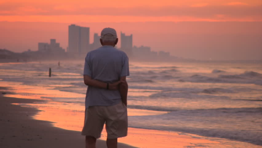 An elderly man walks alone on the Atlantic seashore at sunrise