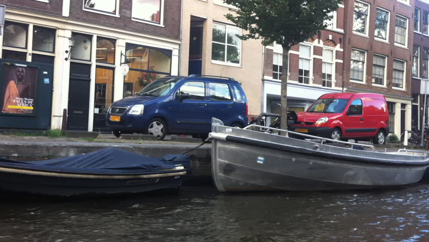 AMSTERDAM - SEPTEMBER 2012: POV from boat as it travels down canals, capturing bicycles, cars,bridges, and houseboats. The canals in Netherlands were dug in 17th century.