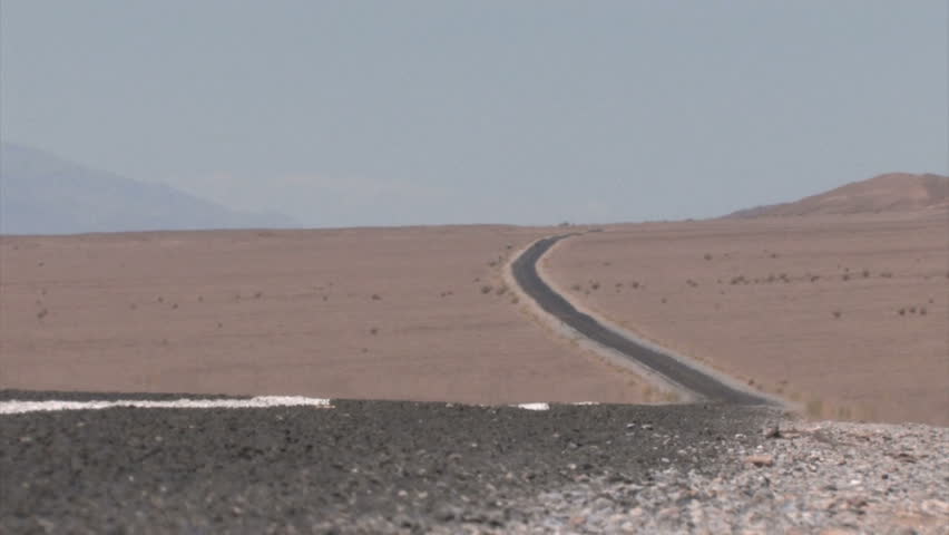 Car in the background on a Highway winding through the Desert with heat haze on the pavement

