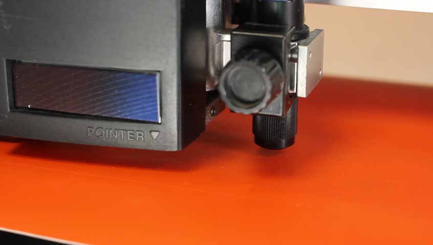 Cutting plotters use knives to cut the letters on orange vinyl film. Three-quarter view close-up
