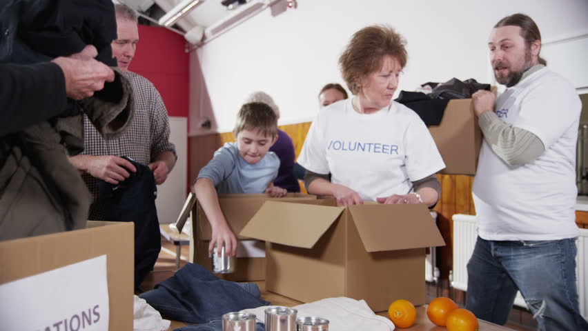 A group of charity workers and community members of all ages are sorting through items of donated food and clothing.