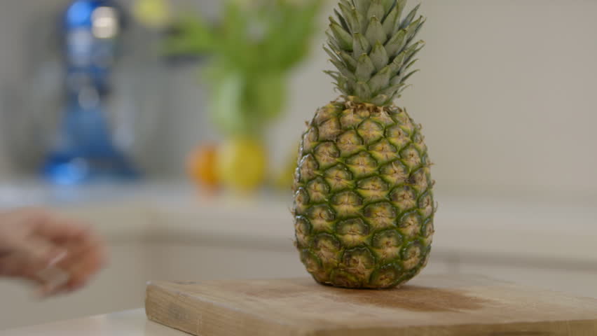 Close shot of woman cutting pineapple in modern kitchen, low depth of field