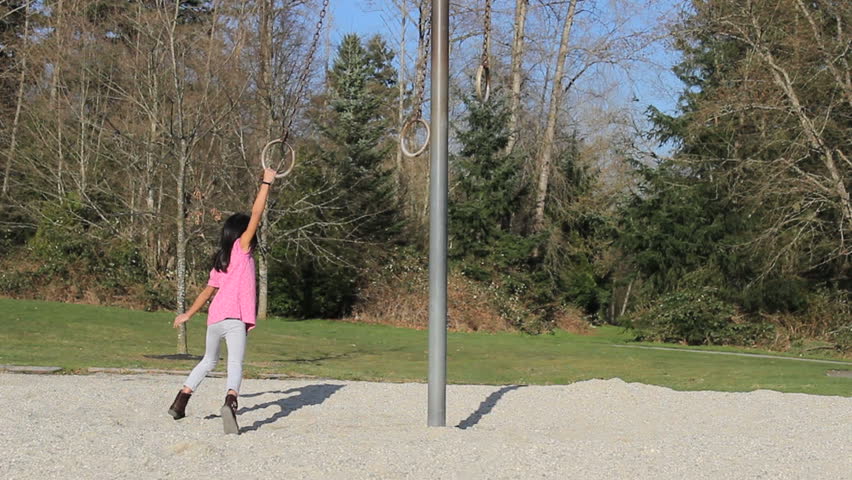 A cute little Asian girl has a fun time playing on the rings at the local playground pretending to be a ballerina.