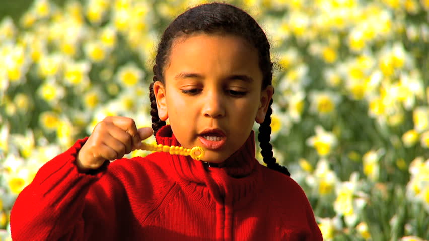 Cute african american child blowing soap bubbles in a field of flowers