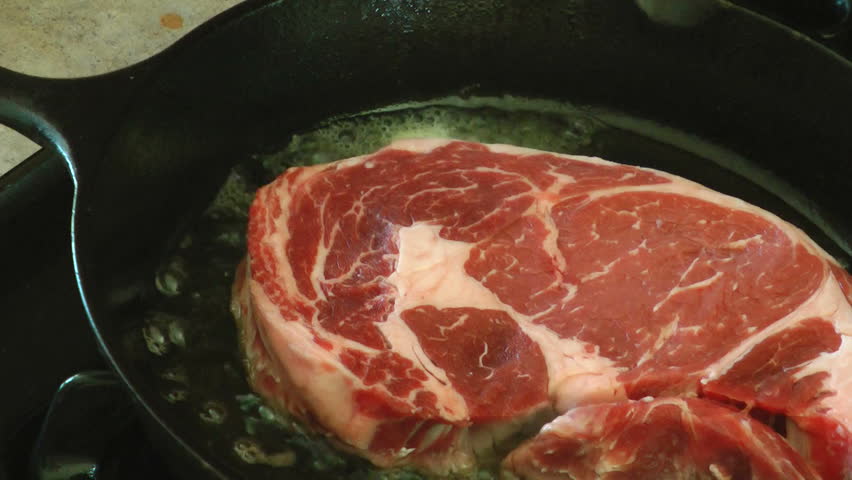 Delicious Rib Eye steak frying in a cast iron pan