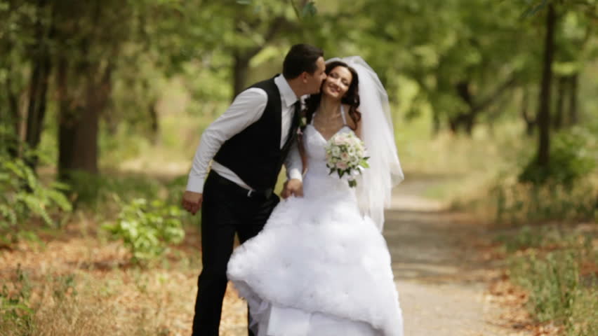 Bride and groom walking in park, kissing