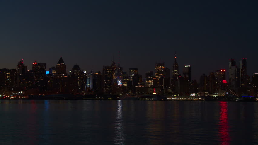 The mid-town Manhattan skyline remains illuminated with lights reflecting off the surface of the Hudson River during the last hour before sunrise in New York City.