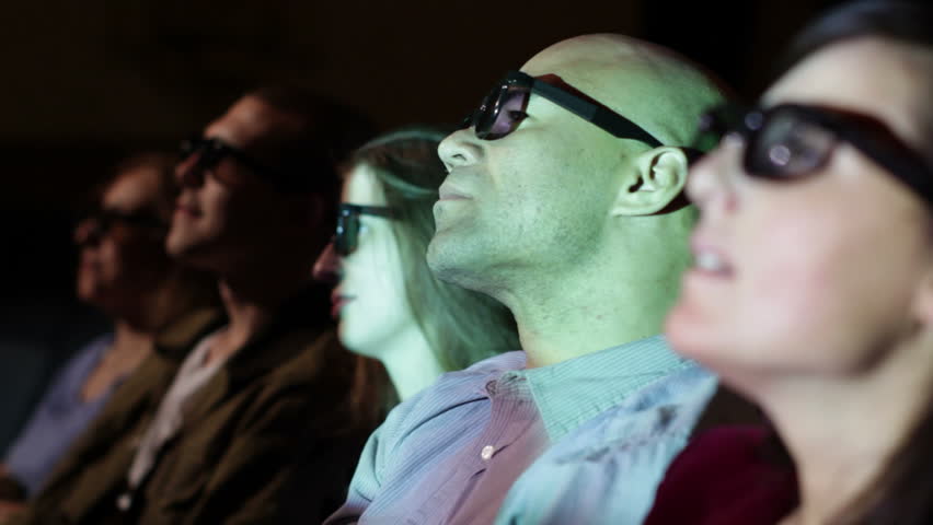 Young man watching a 3D movie with a group of friends. Focus on him with a small dolly move and projections on his face.