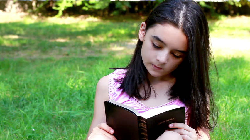 Young Girl reading Holy Bible in summer park