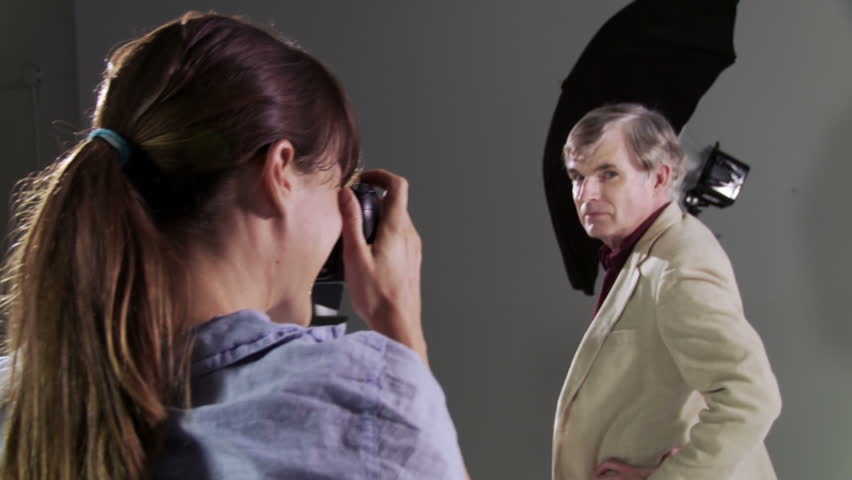 Female photographer takes pictures of male actor/model. Deliberately edgy, hand-held camera in studio with focus on photographer.