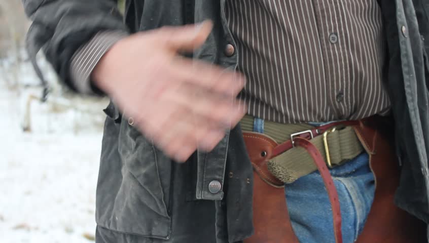 Close up of the waist area. Man wearing long coat shows the revolver on his hip.