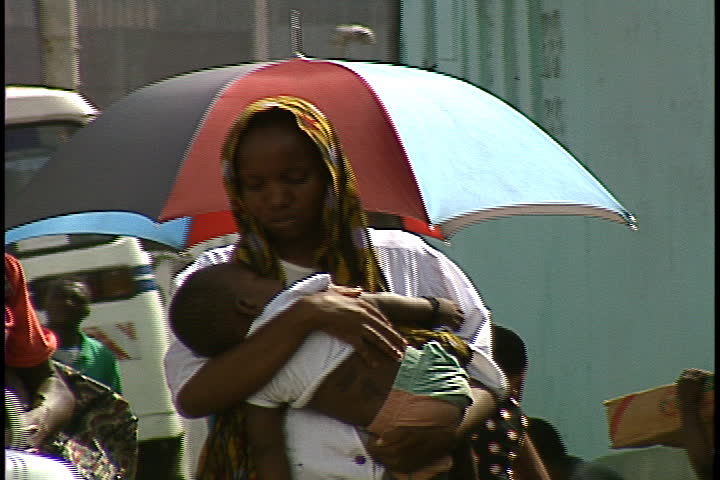 DAR ES SALAAM, TANZANIA - DECEMBER 1, 1998: A woman walks while holding a sleeping child in her arms.