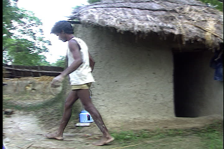 SULTANPUR, INDIA - JULY 28, 1999: Man walks out of house carrying solar powered lantern. He plugs lantern in to be charged, then adjusts solar panel nearby.