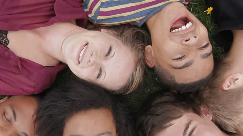 Teens lying on grass - A diverse group of teenagers lying on the grass looking up towards the camera