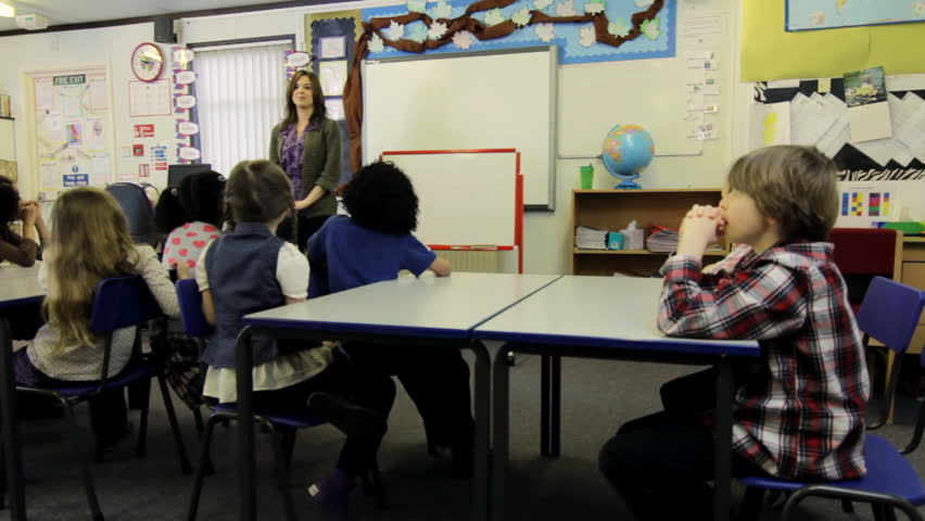 Elementary school class room - a group of primary school children raise their hands to answer the teacher's question