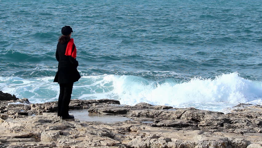Woman with red scarf standing by the sea.

            
