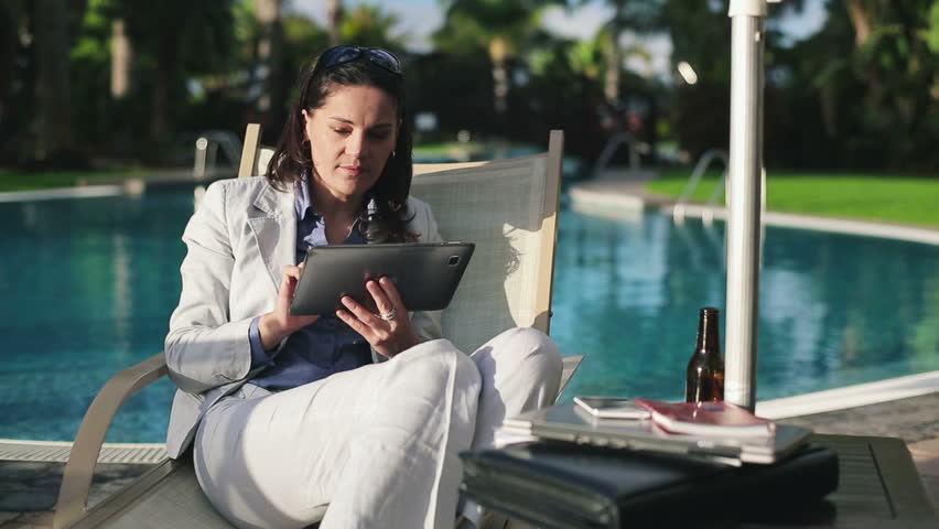 Businesswoman on sunbed using tablet computer by the pool
