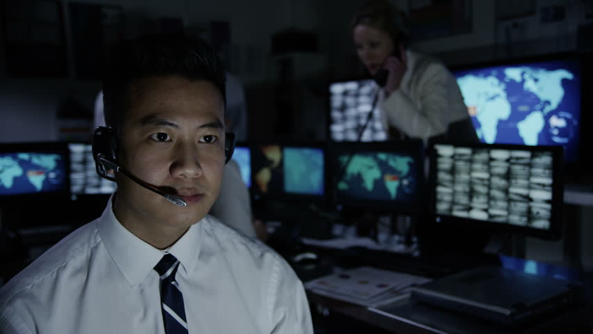 Security worker in a busy system control room is taking calls via a headset and either issuing or receiving instructions. 