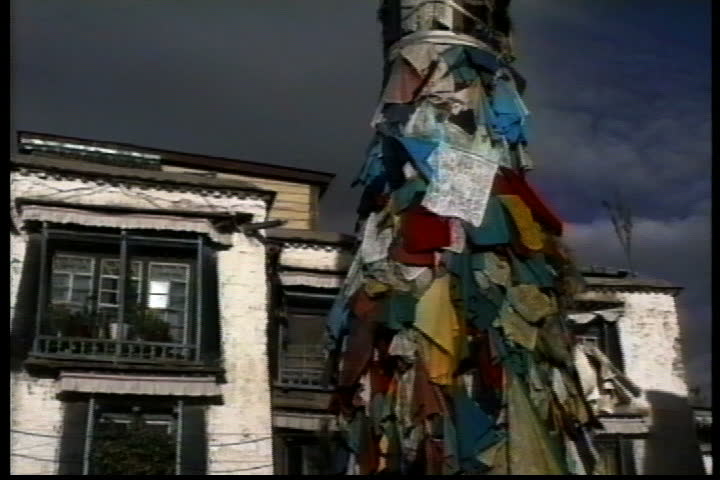 LHASA, TIBET - OCTOBER 01, 1993: Pole covered with prayer flags, camera pans to monks and villagers walking past bonfire.