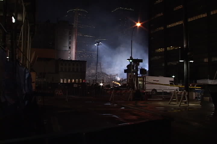 NEW YORK CITY - SEPTEMBER 28, 2001: Smoke rising from World Trade Center site and surrounding skyscrapers at night. Emergency vehicles pass, zoom in to floodlit rubble.