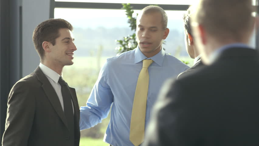 Confident and attractive business team of mixed ethnicity meet and shake hands in the lobby of a busy modern office building. 