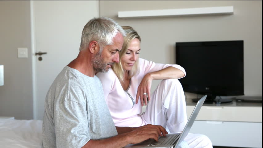 Couple using laptop together and chatting in bedroom