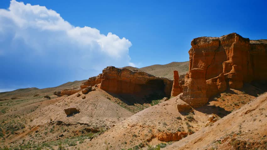 Timelapse over the Charyn (Timerlik) Canyon. Fluffy clouds above red rock mountain peak. Natural landscape erosion and grand canyons with stunning rock formations.