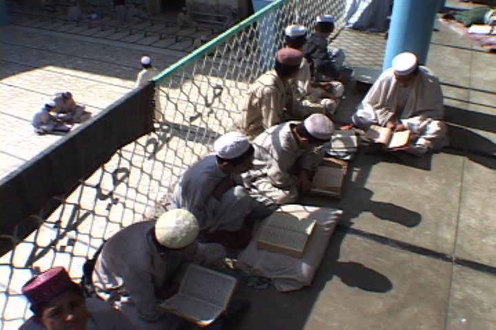 PESHAWAR, PAKISTAN - NOVEMBER 01, 2001: Group of young men in Muslim dress seated in the sun, they rock back and forth as they read the Koran.
