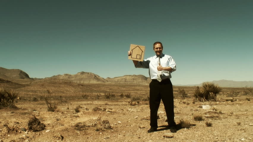 One single businessman in the middle of the desert holding a cardboard sign with an home logo on it