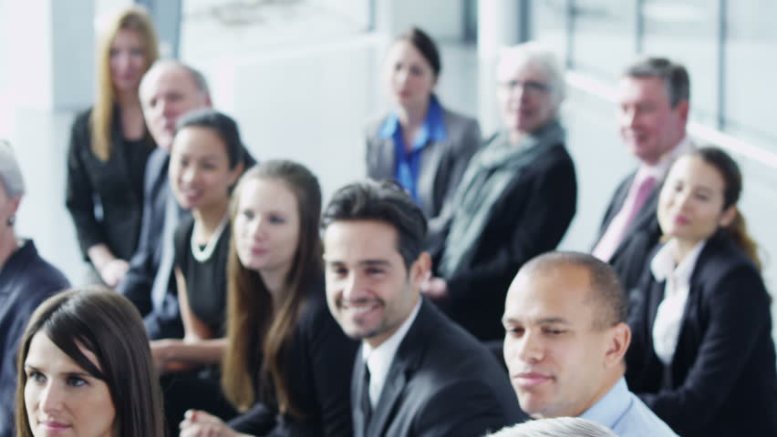 A group of business people of mixed ages are listening to a presentation at a business seminar and asking questions. 