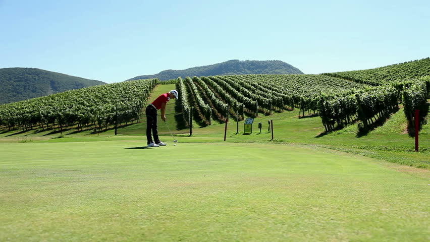 Shot of a woman golfer that hits a white golf ball with a golf club and the beautiful landscape in the background