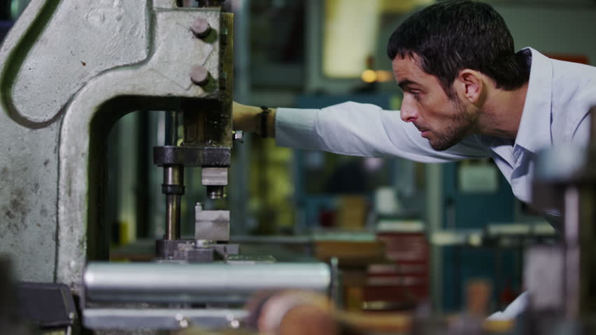 A young professional warehouse or factory manager is checking one of his metalwork machines for an operational fault. In slow motion.