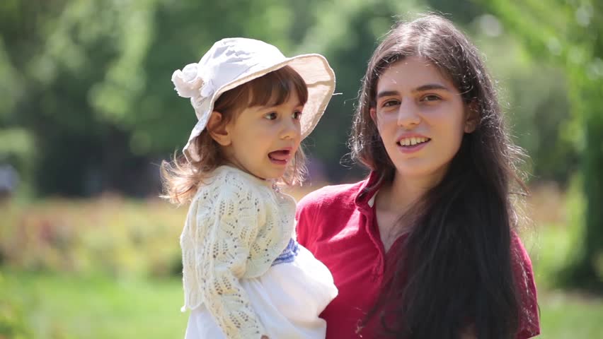 Portrait of brunette young adult mother and little baby girl. Sunny day, outdoor portrait.
