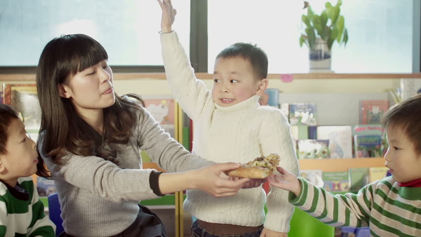 asian kindergarten teacher and her students sharing a pizza together in a classroom in china. dolly shot. 