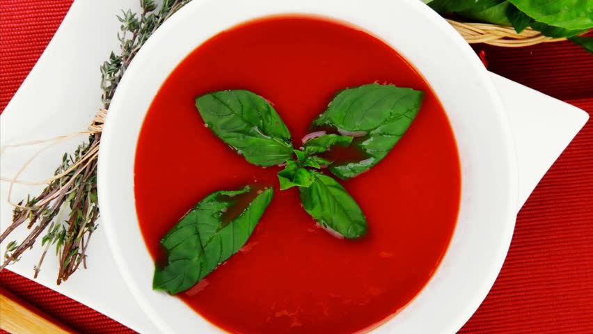 cold fresh diet tomato soup with basil thyme and dry pepper in big bowl over red mat on wood table ready to eat 1920x1080 intro motion slow hidef hd