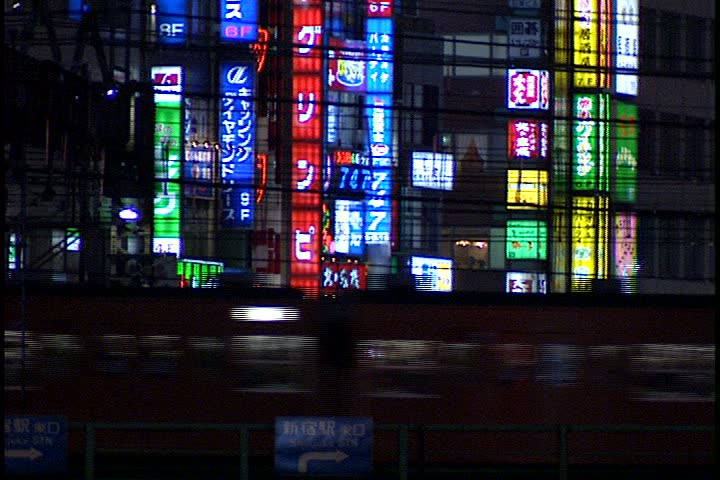 TOKYO - DECEMBER 06, 1996: MS subway train passes in front of glass building with colorful neon signs in reflection.