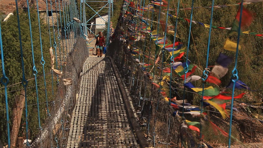 The woman passes through the river on the hinged bridge. Nepal, Himalayas.