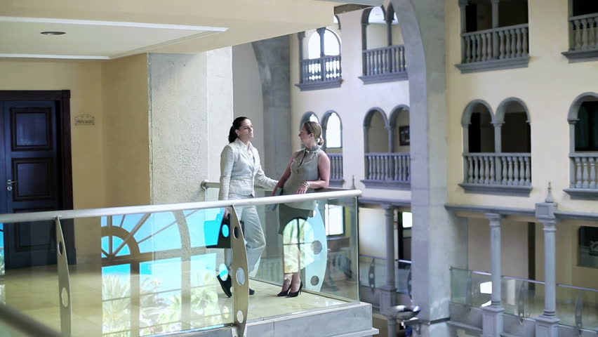 Two businesswoman standing on balcony in the hotel and chatting
